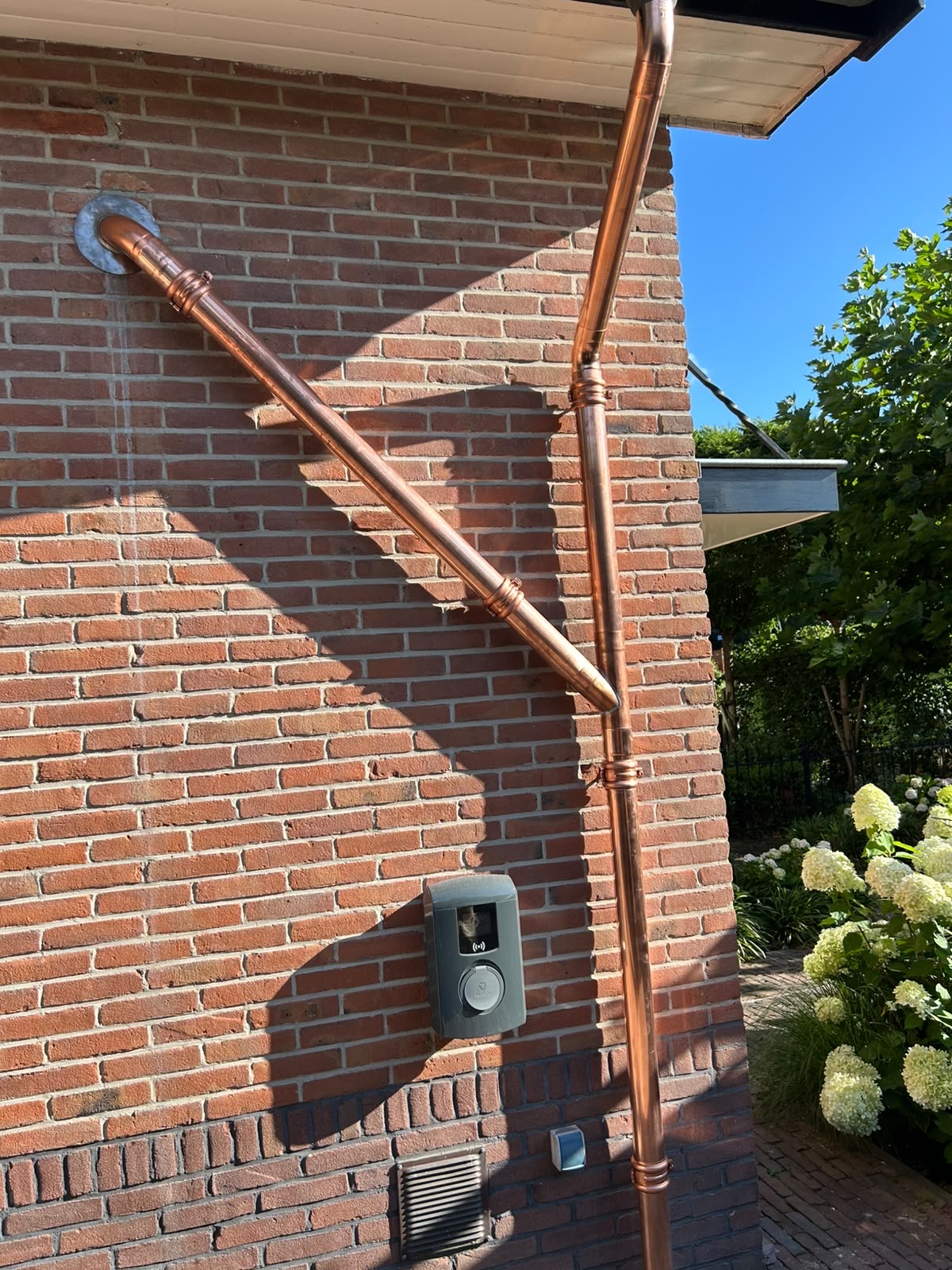 Koperen hemelwaterafvoer met gesoldeerde verbindingen en koperen beugels tegen een bakstenen muur