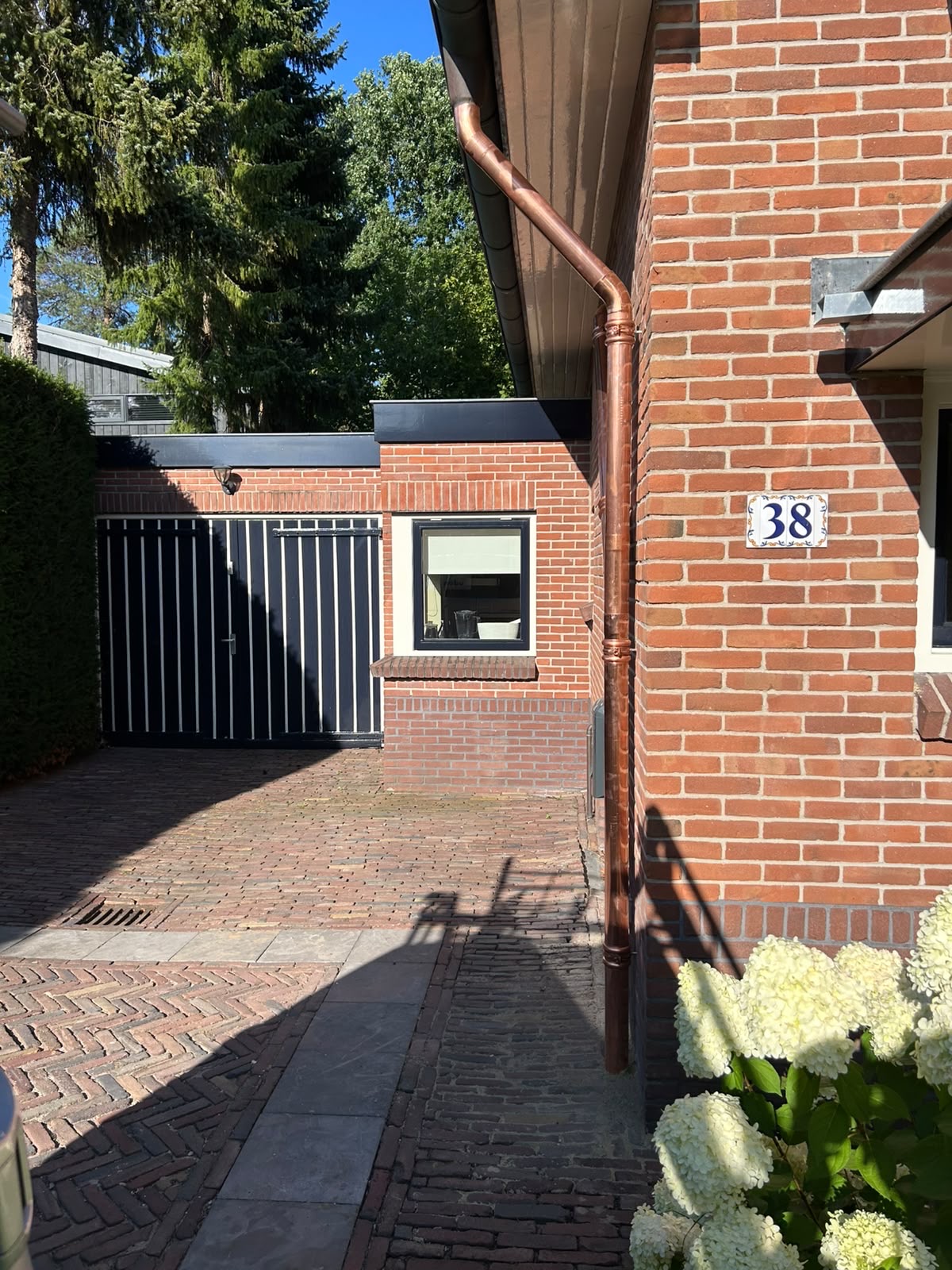 Koperen regenpijp langs de hoek van een woning, met een gebogen aansluiting op de dakgoot