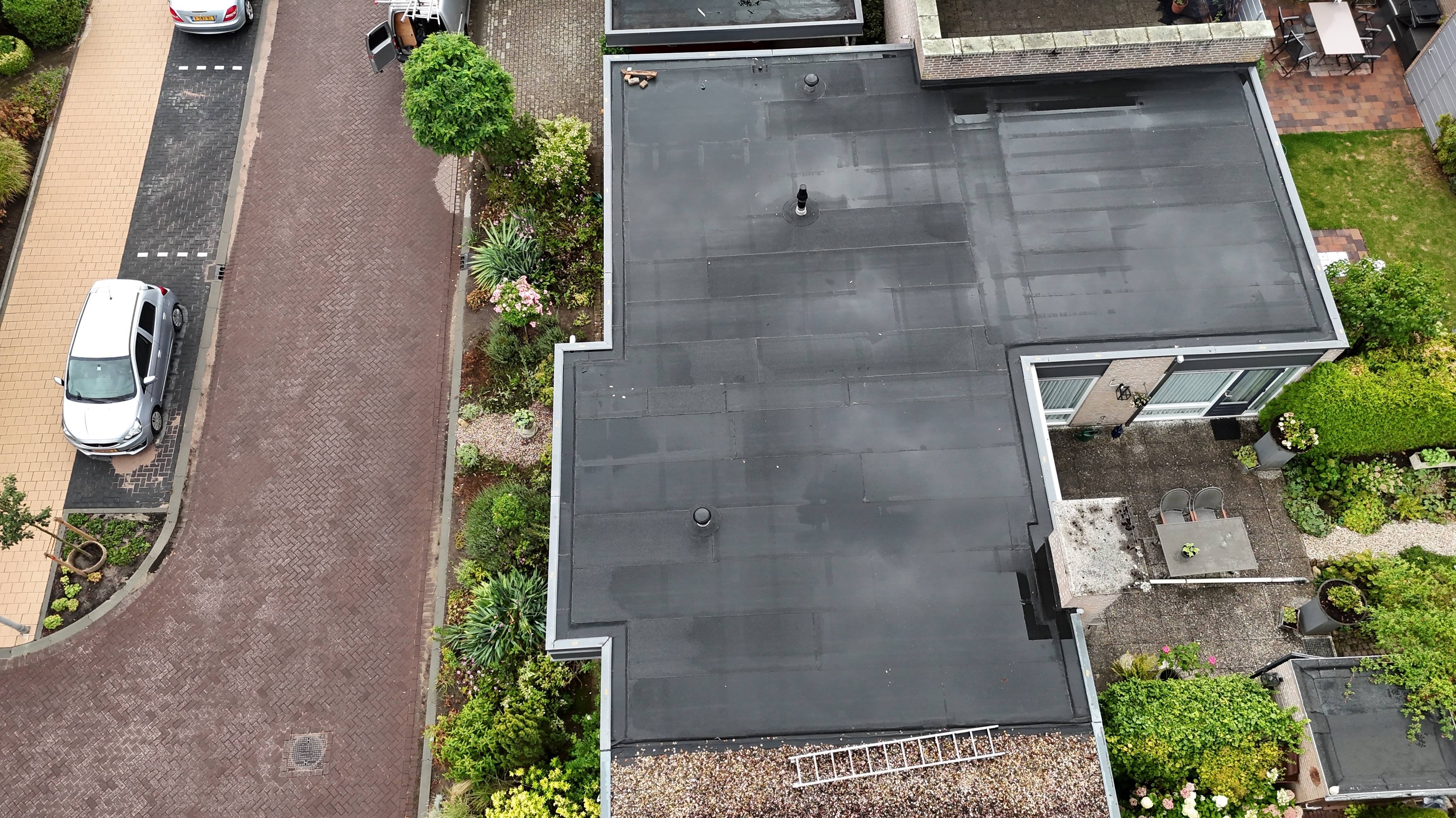 Luchtfoto van een plat dak met nieuwe bitumen dakbedekking, dakrandtrim rondom en twee dakdoorvoeren
