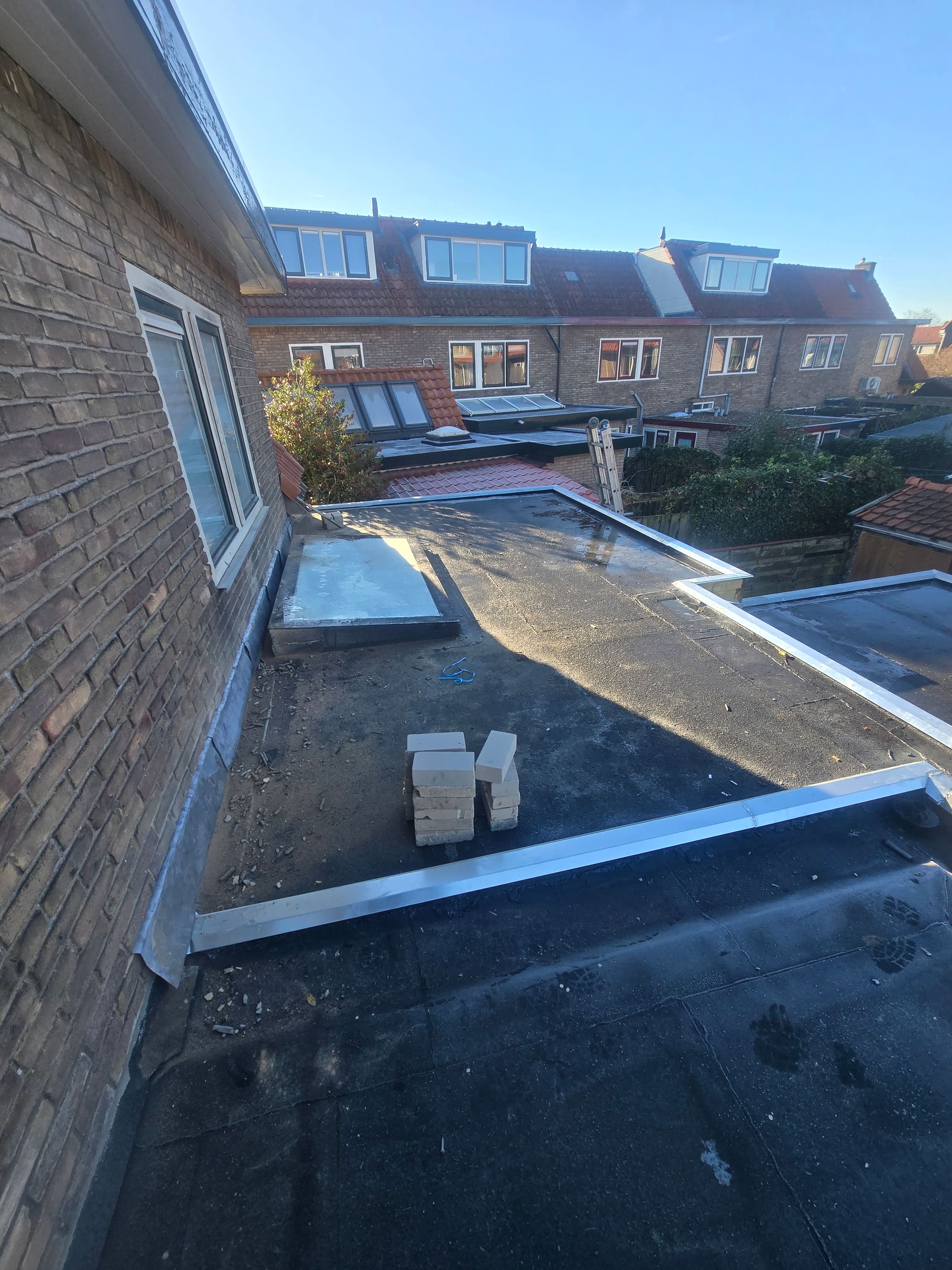 Plat dak van een aanbouw met nieuwe zinken dakrand, met uitzicht over de achtertuinen